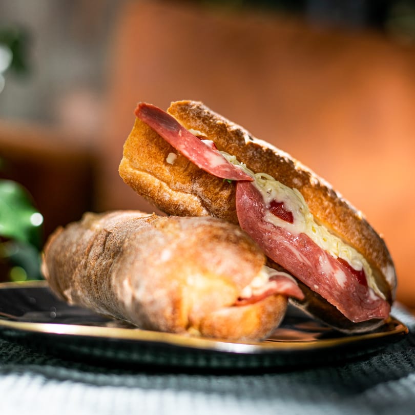 Two salami and cheese sandwiches on crusty bread, stacked on a dark plate.