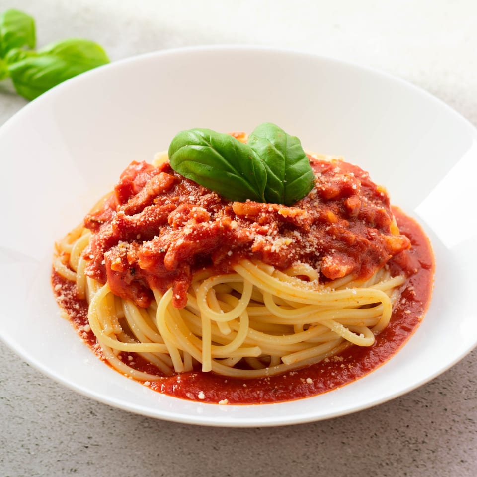 Spaghetti with rich red tomato sauce, grated Parmesan cheese, and fresh basil in a white bowl.