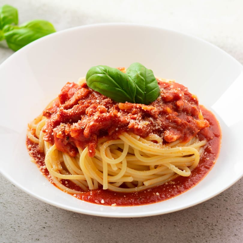 Spaghetti with rich red tomato sauce, grated Parmesan cheese, and fresh basil in a white bowl.