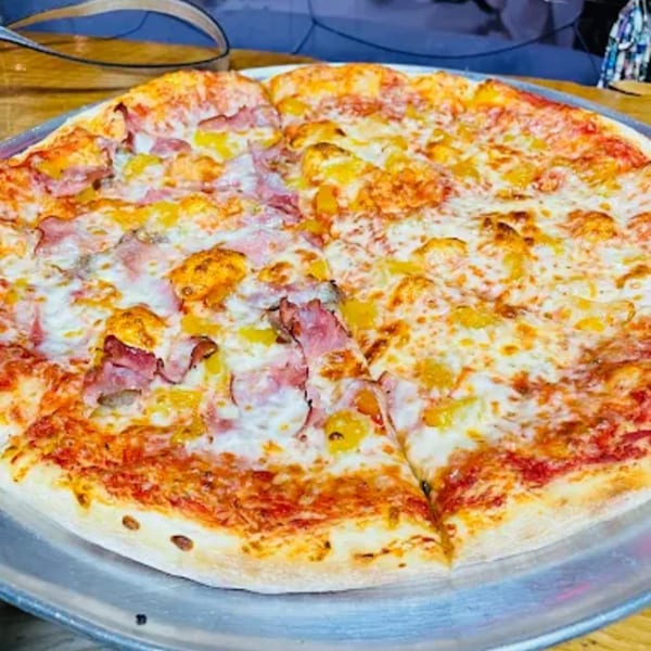 A whole pizza with ham and pineapple toppings, served on a metal tray.