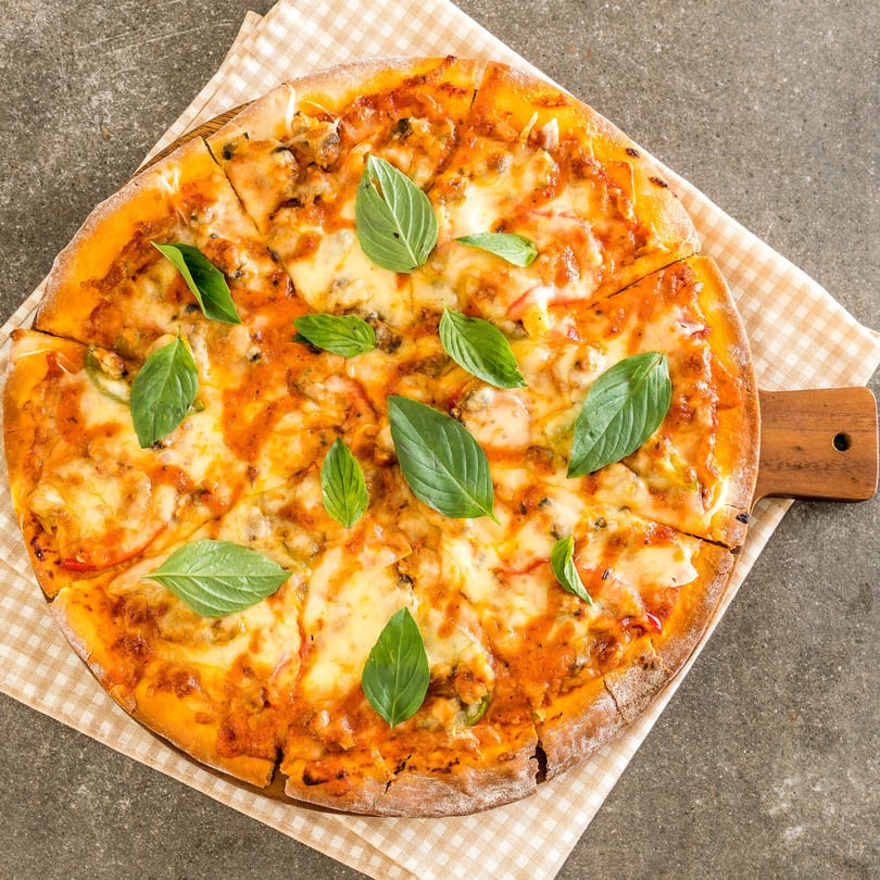 A sliced pizza with melted cheese, tomato sauce, and fresh basil leaves on a wooden board.