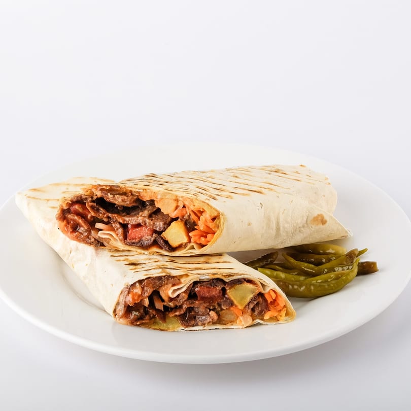 Two shawarma wraps, cut in half, revealing meat, vegetables, and sauce, served with pickled peppers.