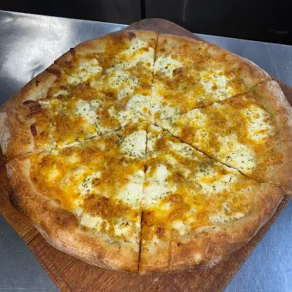 A freshly baked white pizza, topped with melted cheese and herbs, sliced on a wooden board.